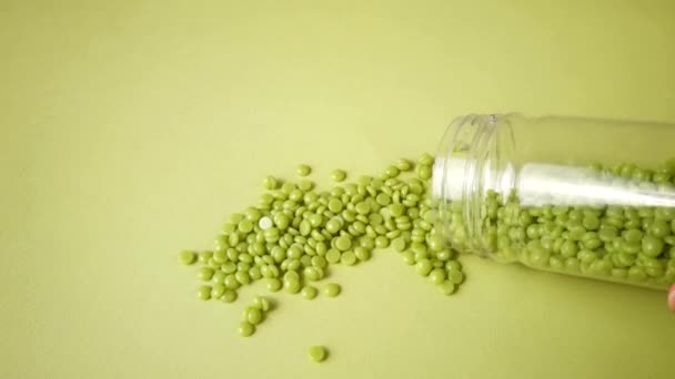 La cera depilatoria con aloe in granuli è versata da un vaso su uno sfondo verde chiaro. Epilazione, depilazione, depilazione indesiderata. Vista dall'alto. — Video Stock