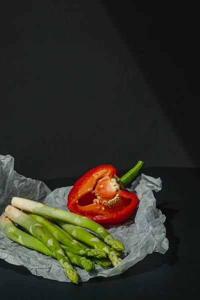 鲜绿色的芦笋和一半红甜的胡椒粉躺在白色羊皮纸上 背景是深灰色的 适当的营养生活方式 案文的位置 — 图库照片