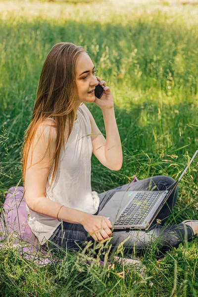 Dziewczyna Siedzi Trawie Pracuje Laptopie Rozmawiam Przez Telefon Wolny Strzelec — Zdjęcie stockowe