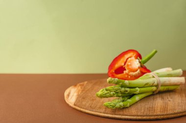 Sebzeler ahşap bir tahtada bulunur: domates, kuşkonmaz, salatalık, kırmızı çan biberi. Kahverengi, açık yeşil arka plan. metin için yer