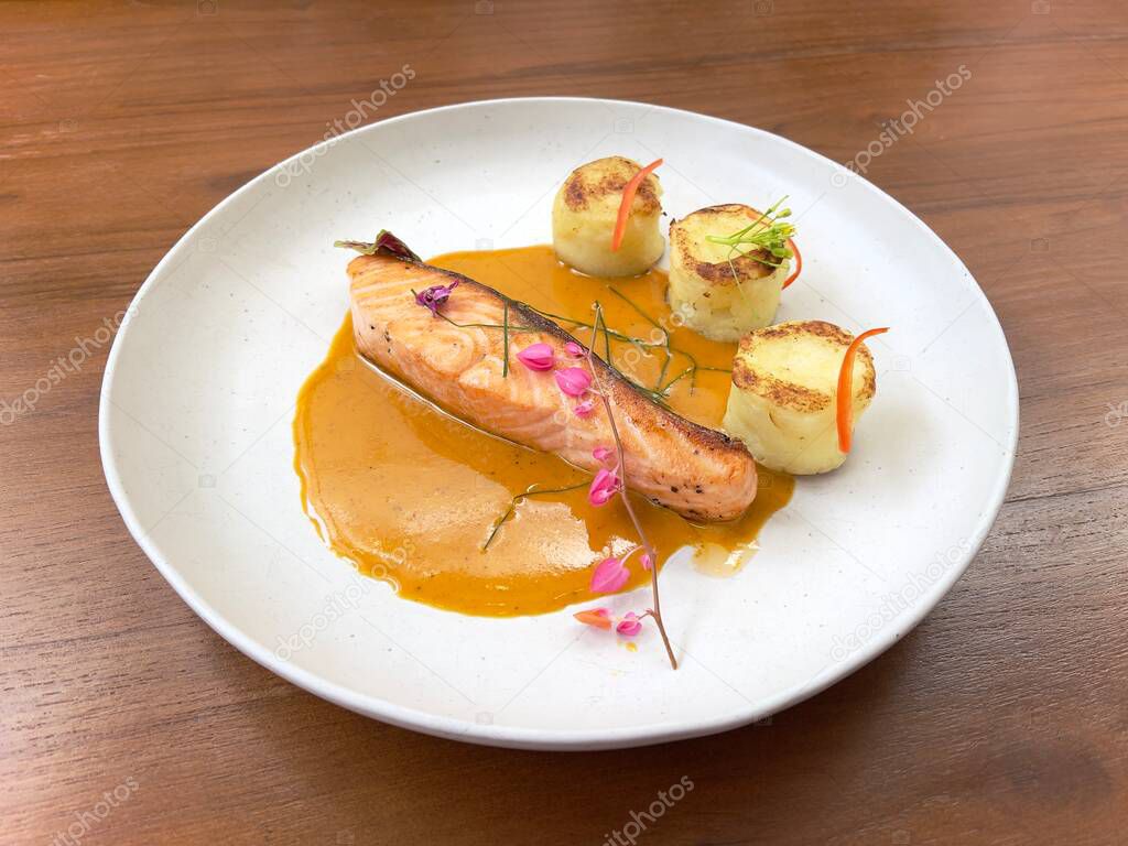 Salmon steak and red curry sauce, served with mashed potatoes and decorated with edible flowers and leaves. Fine dining main course. Selective focus