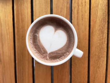 Hot chocolate, top view. Hot drink with heart shaped latte art in white mug on wooden table, top view.