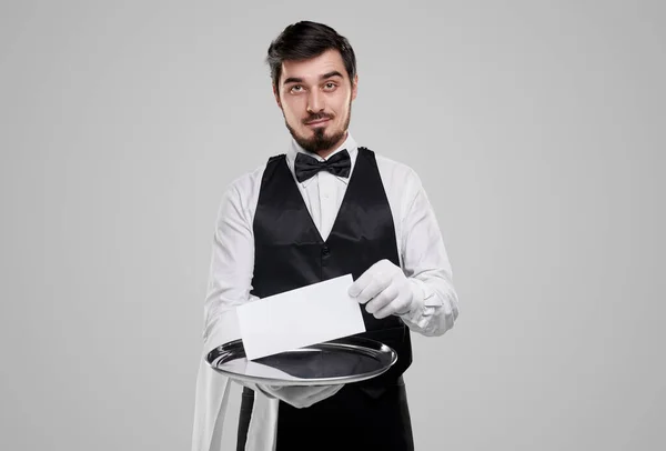 Garçom elegante com papel vazio no fundo cinza — Fotografia de Stock