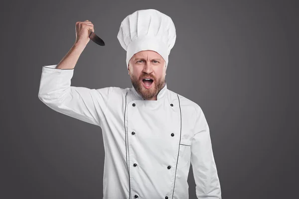 Chef irritado com faca no fundo cinza — Fotografia de Stock