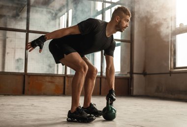 Sporcu spor salonunda kettlebell ile çalışıyor.