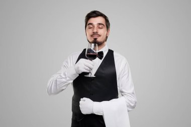 Şık üniformalı garson şarabın tadını çıkarıyor.
