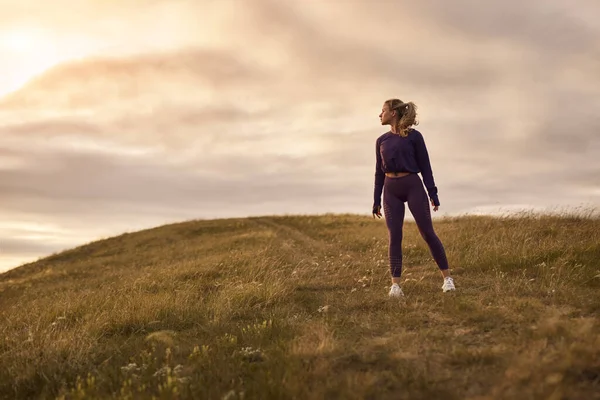 Αθλητική γυναίκα στέκεται στο λόφο στο ηλιοβασίλεμα — Φωτογραφία Αρχείου
