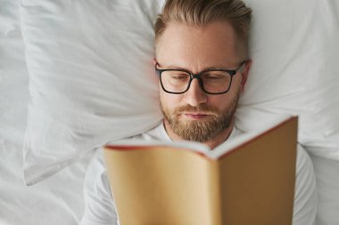 Yatakta kitap okuyan düşünceli adam.