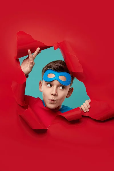 Superbohater patrząc przez podarty czerwony papier — Zdjęcie stockowe
