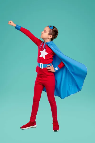 Little brave superhero kid standing with raised arm in studio — Stock Photo, Image