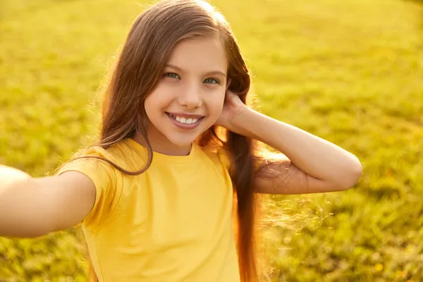 Радісна дівчина торкається волосся і посміхається на камеру, приймаючи селфі в природі — стокове фото