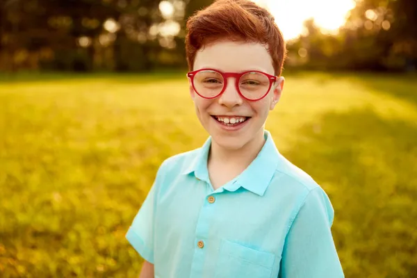 Opgewonden roodharige jongen in trendy brillen glimlachend naar camera in de natuur — Stockfoto
