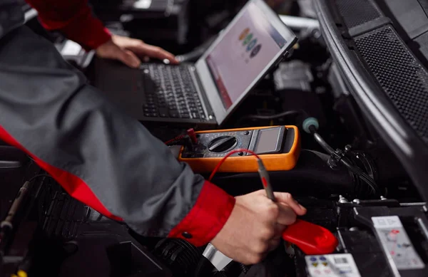 Anonymous repairman doing car diagnostic with multimeter and netbook