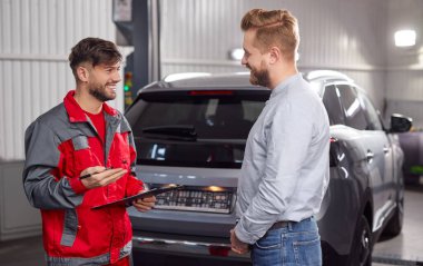 Tamir edilmiş arabanın yanındaki garajda sohbet etmekten memnun olan tamirci ve müvekkil