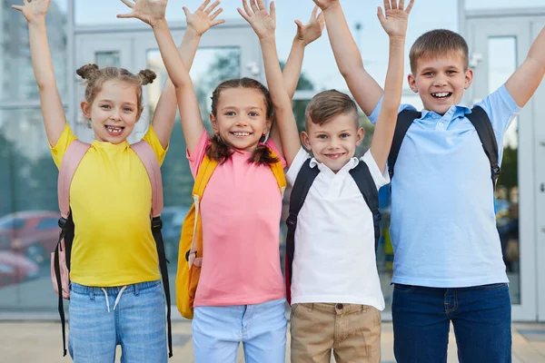 Веселі учні з піднятими руками біля будівлі школи — стокове фото