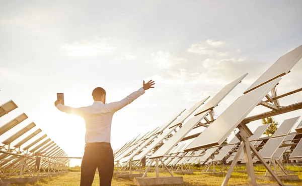 Entusiástico engenheiro masculino espalhando armas enquanto estava em pé na central de energia solar — Fotografia de Stock