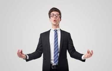 Takım elbiseli komik erkek girişimci, Mudra elleriyle meditasyon yapıyor ve iş yerindeki stresi azaltmak için gri arka planda yoga yapıyor.