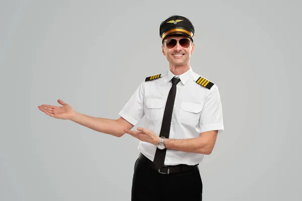 Smiling pilot pointing aside on gray background