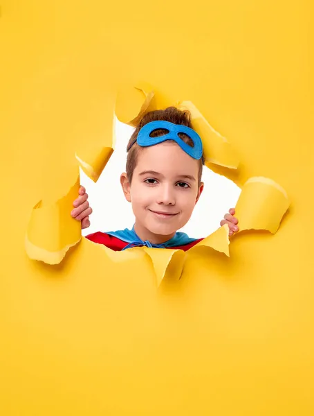 Superhero child looking through torn paper — Stock Photo, Image