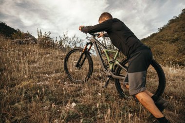 Genç sporcu bisikletle çimenli dağa tırmanıyor.