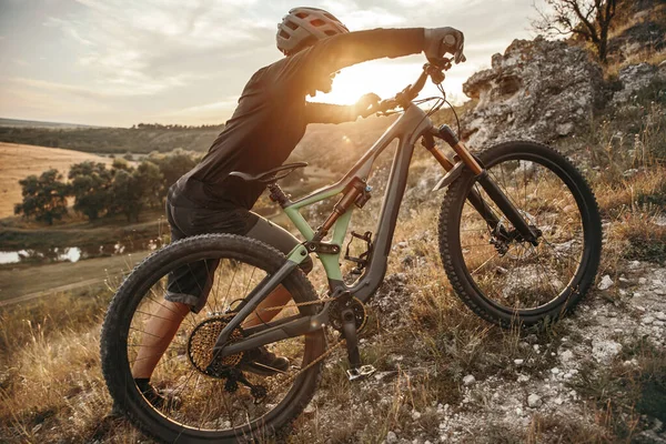 Giovane ciclista di sesso maschile rotolamento bici sul pendio erboso di montagna al tramonto — Foto Stock