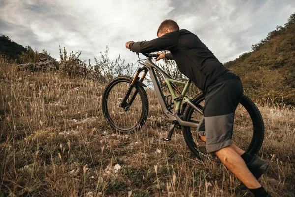 Giovane ragazzo sportivo ascendente montagna erbosa con bicicletta — Foto Stock