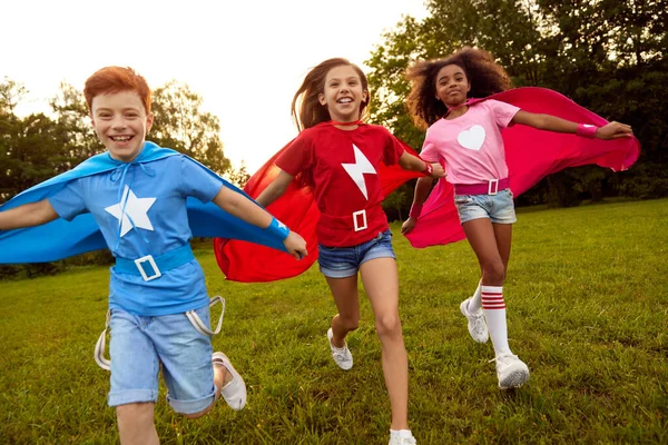 Bezstarostné rozmanité superhrdinové děti běží podél louky — Stock fotografie