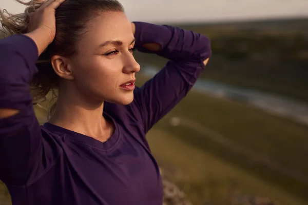 Verträumte junge Frau berührt Haare und bewundert die Natur bei Sonnenuntergang — Stockfoto