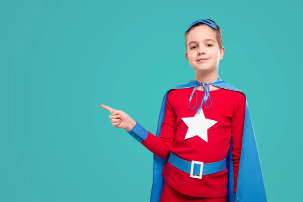 Smiling superhero child pointing away — Stock Photo, Image