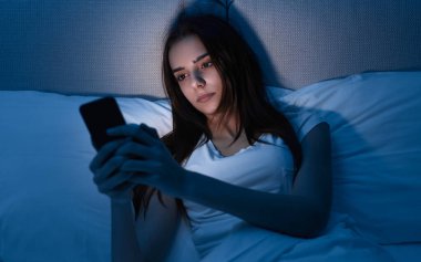 Gece yatakta akıllı telefon kullanan bir kadın.