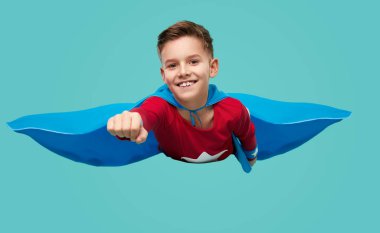 Smiling boy in superhero costume flying to camera