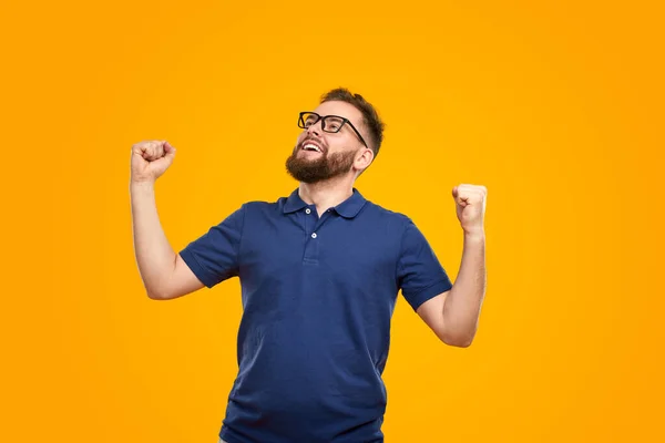 Satisfied young guy with clenched fists celebrating victory in yellow studio — ストック写真