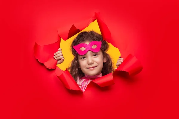 Delighted superhero girl looking through torn paper — Stockfoto