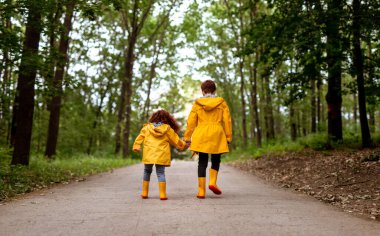 Redhead siblings in yellow raincoats walking in park