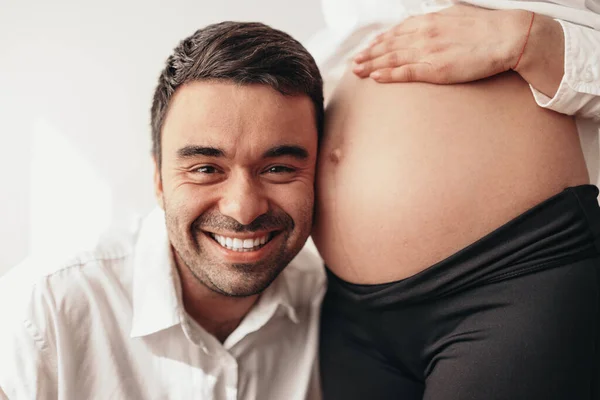 Glücklich lächelnder ethnischer Mann lehnt Ohr am Bauch der schwangeren Frau — Stockfoto