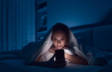Gece yatakta akıllı telefonlara bakan bir kadın.
