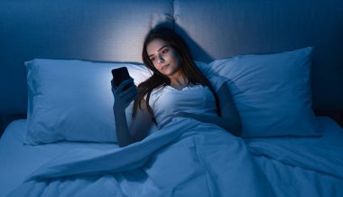 Genç bayan gece yatakta akıllı telefon kullanıyor.