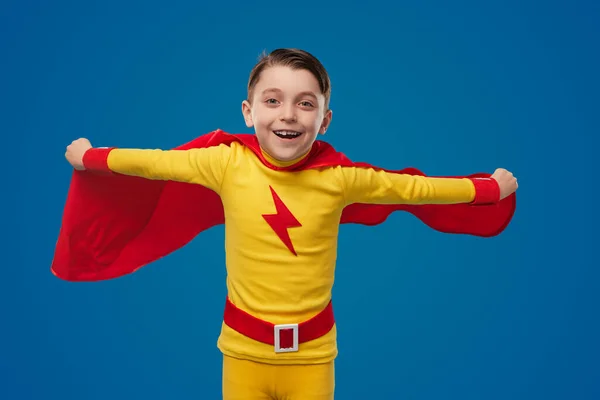 Fröhlicher Junge in Superhelden-Umhang fliegt im Studio — Stockfoto