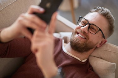 Kanepede akıllı telefon kullanan içerik adamı.