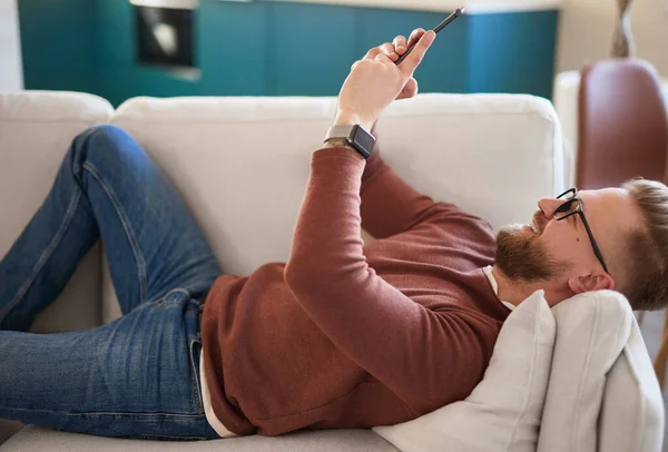 Wesoły człowiek przeglądający smartfona na sofie — Zdjęcie stockowe