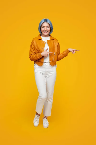 Веселая молодая женщина, указывающая в сторону, стоя в желтой студии — стоковое фото