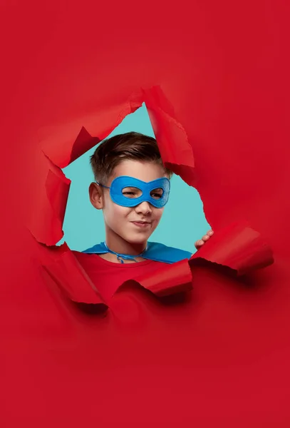 Superhelden-Kind blickt durch Loch in zerrissenem Papier — Stockfoto
