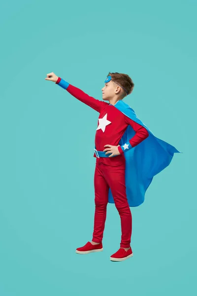 Superhéroe niño fingiendo vuelo contra fondo azul — Foto de Stock