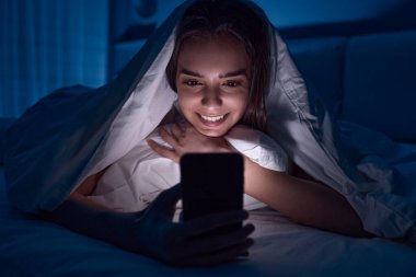 Geceleri cep telefonundan video izleyen mutlu bir kadın.