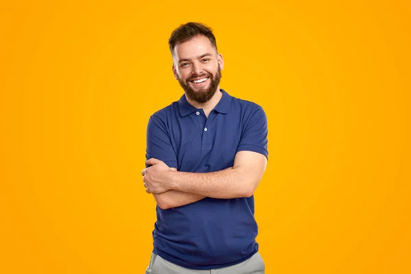 Позитивний молодий бородатий чоловік стоїть зі складеними руками і посміхається — стокове фото