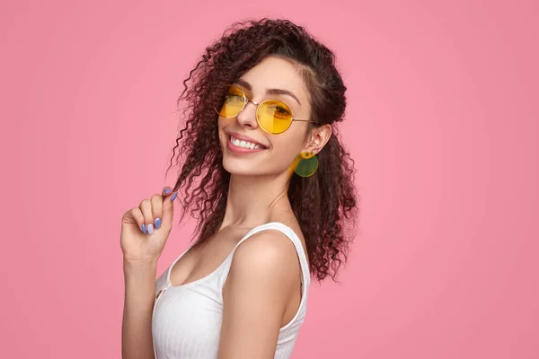 Stylische selbstbewusste Dame mit trendiger Sonnenbrille lächelt im rosa Studio — Stockfoto
