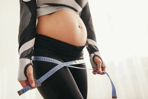 Femme enceinte anonyme faisant des mesures avec du ruban adhésif après l'entraînement — Photo