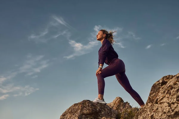 Spor kadını antrenman sırasında bacaklarını kayaların üzerinde açıyor. — Stok fotoğraf