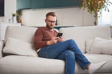 Evde akıllı telefonlara bakan meşgul bir adam var.