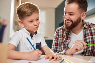 Baba ve oğul evde birlikte resim çiziyorlar.
